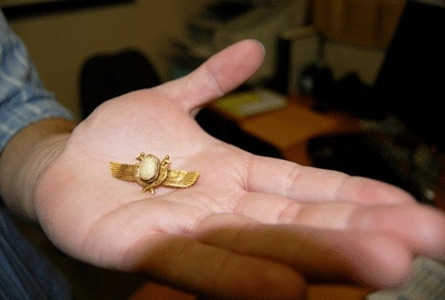 Thrift shop assistant manager Logan Ens holds a 14 karat gold Egyptian winged scarab brooch