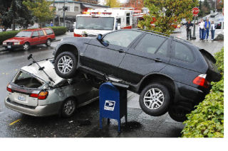 A BMW sport utility vehicle rests on top of a U.S. Postal Service mailbox and a parked Subaru after driving over a parking lot retaining wall along 76th Avenue S.E. in the Town Center on Halloween. Go to page A7 for the full story.