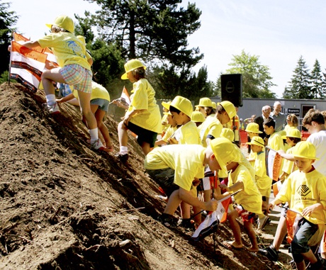 Children from the Mercer Island Boys & Girls Club clamber up a mountain of dirt to plant their flags during the groundbreaking ceremony for the soon-to-be PEAK facility on Monday morning