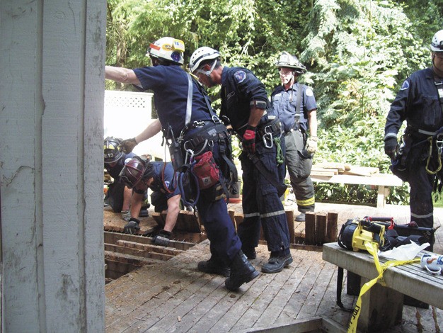 Members of the Seattle and Mercer Island fire departments work to free a man stuck in a trench under the deck of a home on Friday afternoon.