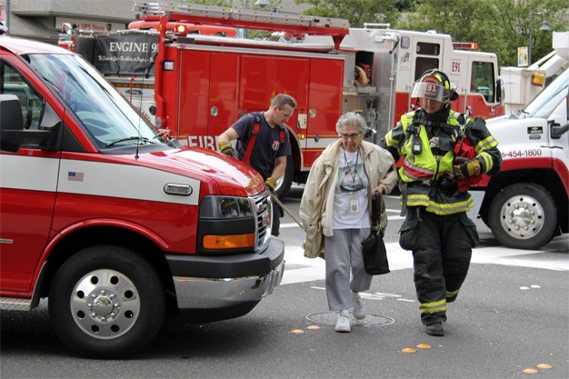 A firefighter leads the woman whose car hit utility equipment in front of The Mercer after she ran a red light and was struck by a pickup truck. The woman remained in her car until Puget Sound Energy shut off local power and determined it was safe.