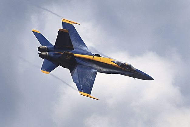 Condensation trails stream off the wing tips and leading edges of Blue Angel No. 5 during Saturday's performance