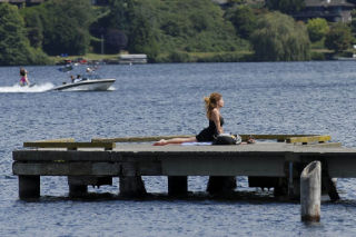 Island resident Soleil Hepner practices yoga as boaters take a wakeboard run during a break from the rain at the Luther Burbank Park on Mercer Island