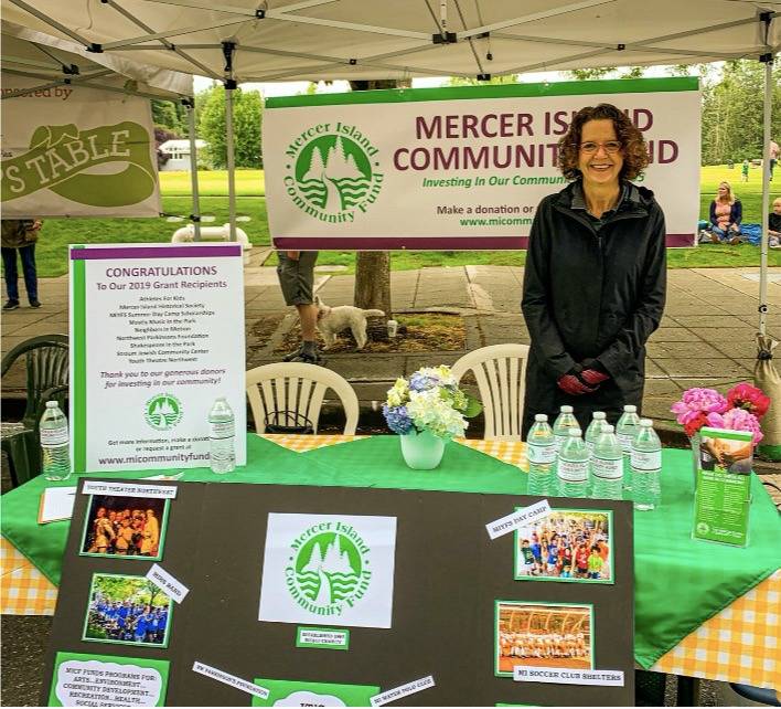 Mercer Island Community Fund board member Sarah Cox represents the fund at a table at the Mercer Island Farmers Market, pre-COVID. Photo courtesy of Erin Sirianni’s My MI blog